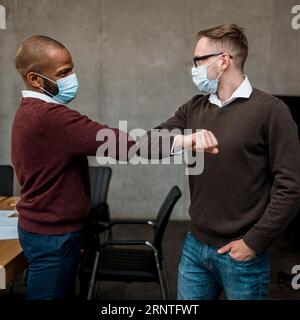 Seitenansicht Männer Ellbogen salutieren einander während des Treffens tragen medizinische Masken Stockfoto