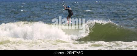 Rückansicht eines männlichen Kitesurfers, der über brechende Wellen im Ozean vor der Küste von Long Island New York reitet. Stockfoto