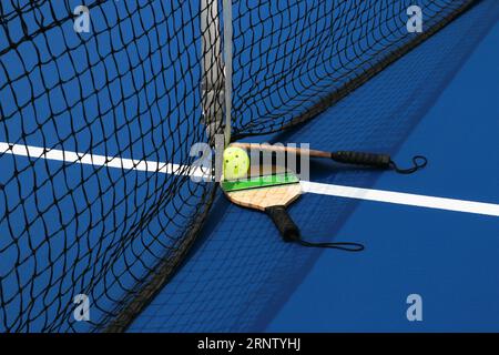 Seitenansicht von zwei Pickleball-Paddles und einer gelben Schlagkugel auf einem blauen Platz aus nächster Nähe. Stockfoto