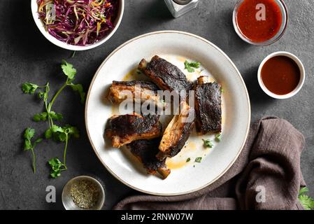 Schweinerippen auf Teller auf dunklem Steinhintergrund. Draufsicht, flach Stockfoto