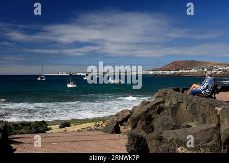 Ein Paar sitzt auf einer Bank in der Nähe von Marina Rubicon und genießt den Meerblick, Playa Blanca, Lanzarote, Kanarische Inseln, Spanien Stockfoto