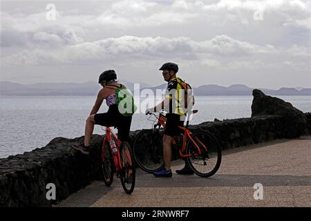 Mann und Frau Radfahrer genießen die Aussicht, Küstenweg, Los Coloradas nach Playa Blanca, Lanzarote, Kanarische Inseln, Spanien Stockfoto