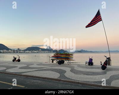 Rio de Janeiro, Brasilien: Surfbretter stapeln sich auf einem Wagen bei Sonnenuntergang am Strand von Ipanema mit dem ikonischen grafischen Bürgersteig entlang der Avenida Atlantica Stockfoto