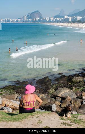 Rio de Janeiro, Brasilien: Frau mit ihrem Hund genießt den Panoramablick auf die Skyline der Stadt mit Wolkenkratzern und dem kristallklaren Wasser des Leme-Strandes Stockfoto