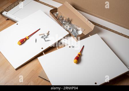 Ein Schlitz- oder Schlitzschraubendreher und ein Stapel von Teilen eines neuen Möbels, verschiedene Montagemöbelbeschläge. Stockfoto