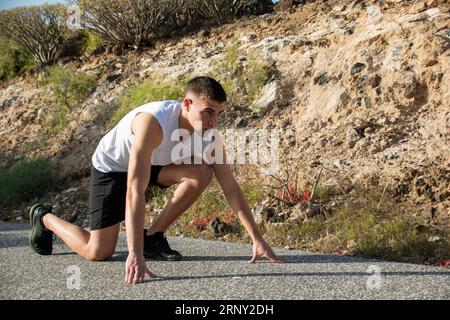 Nahaufnahme eines konzentrierten jungen Kaukasiers, der den Start eines Leichtathletikrennens simuliert Stockfoto