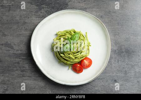 Leckere Tagliatelle mit Spinat und Tomaten auf grauem Tisch serviert, Blick von oben. Exquisite Präsentation von Nudelgerichten Stockfoto