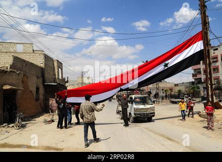 Bilder des Tages (180414) -- DOUMA, 14. April 2018 -- Syrier hissen am 14. April 2018 eine große syrische Nationalflagge im Damaskus-östlichen Duma-Bezirk in Syrien. Die russische Militärpolizei und die syrischen Polizeikräfte begannen ihren Einsatz in ganz Duma gemäß dem am 8. April erzielten Abkommen, nach dem die syrischen offiziellen Institutionen nach Duma zurückkehren werden. ) (Zjl) SYRIEN-DAMASKUS-DOUMA-RUSSLAND-EINSATZ AmmarxSafarjalani PUBLICATIONxNOTxINxCHN Stockfoto