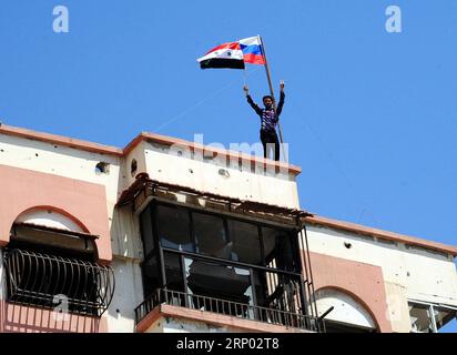 (180414) -- DOUMA, 14. April 2018 -- Ein syrischer Polizist hält am 14. April 2018 syrische und russische Nationalflaggen im Damaskus-östlichen Duma-Bezirk in Syrien. Die russische Militärpolizei und die syrischen Polizeikräfte haben gemäß dem am 8. April erzielten Abkommen, nach dem die syrischen offiziellen Institutionen nach Duma zurückkehren werden, mit dem Einsatz in ganz Duma begonnen.) (Zjl) SYRIEN-DAMASKUS-DOUMA-RUSSLAND-EINSATZ AmmarxSafarjalani PUBLICATIONxNOTxINxCHN Stockfoto