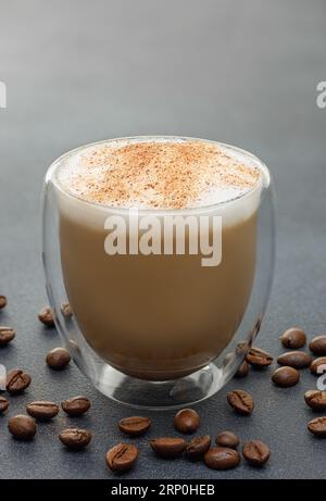 Cappuccino in Glasbecher und Kaffeebohnen auf grauem Tisch Stockfoto