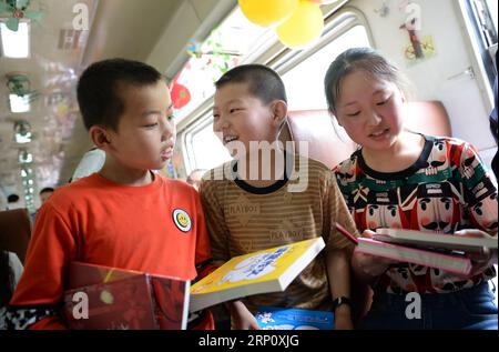 (180529) -- XI AN, 29. Mai 2018 -- Studenten erhalten neue Bücher an den Sonderwagen der Studenten im Zug Nr. 6063 in China, 27. Mai 2018. Der Zug Nr. 6063, der 38 Stationen entlang der Strecke von Baoji der Provinz Shaanxi und Guangyuan der Provinz Sichuan verbindet, bedient Tausende von Schülern, die in Bergregionen leben und jede Woche von Schulen nach Hause pendeln müssen. Zur Verbesserung der Leistungen für die Schülerpassagiere wurden Ende 2017 Sonderwagen mit größeren Schreibtischen und einer Bibliothek in Betrieb genommen. Mit dem Beginn des diesjährigen Internationalen Kindertages, über 300 Stockfoto