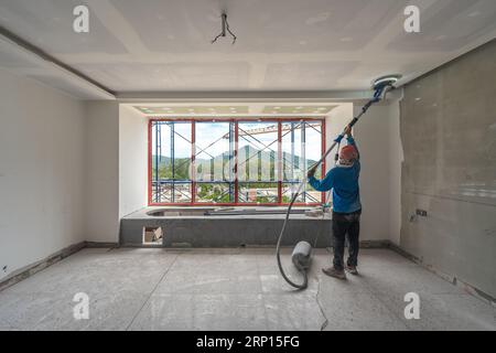 Arbeiter, der Sand- und Zementestrichterwände auf der Baustelle durchführt und poliert Stockfoto