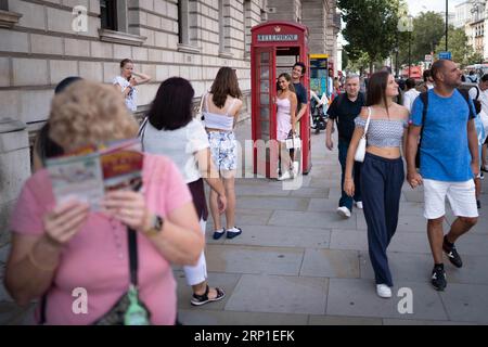 Touristen und Besucher in London lassen sich in einer roten Telefonbox auf Whitehall in Westminster fotografieren, da die Beliebtheit der berühmten Stände im Zeitalter der sozialen Medien mit ihrem 100. Jahrestag andauert. Die berühmte rote Telefonbox wurde von dem Architekten Sir Giles Gilbert Scott für einen Wettbewerb im Jahr 1924 entworfen. Bilddatum: Donnerstag, 21. August 2023. Stockfoto