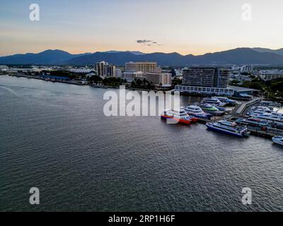 Drohne bei Sonnenuntergang in Cairns Marina und Esplanade mit orangefarbenem Himmel und Bergkulisse Stockfoto