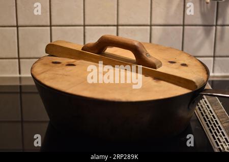 Zubereitung von Dampfnudeln in rustikaler alter Dampfnudelpfanne mit Holzdeckel, typisch bayerische Küche, Deutschland Stockfoto