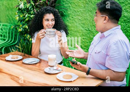Lächelnde Freunde reden und Kaffee am Tisch genießen. Das Konzept von Freunden, die einen guten Kaffee genießen. Zwei glückliche Freunde trinken einen Kaffee und reden Stockfoto