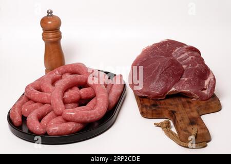 Frische hausgemachte Würstchen auf einem schwarzen Teller und Rinderfilet auf einem Holzbrett auf weißem Hintergrund Stockfoto