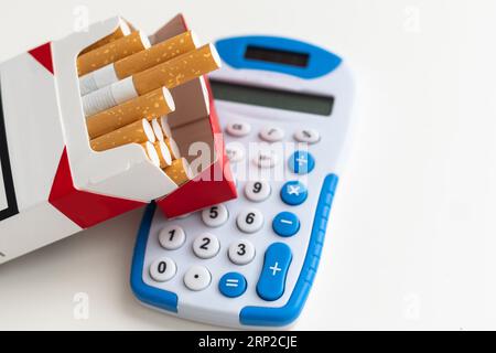 Nahaufnahme auf Rechner mit Ziffern auf Display, Zigarettenpackung und Feuerzeug auf weißem Hintergrund, Rauchkostenkonzept Stockfoto