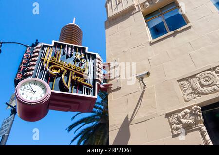 Retro-Hollywood-Zeitschild mit Uhr und Palme vor dem Hintergrund eines historischen Gebäudes in Los Angeles, Kalifornien. Stockfoto