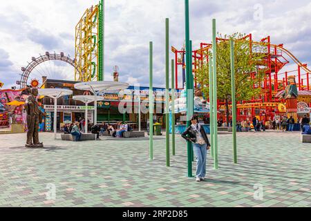 Frau, lächelnd, gegen einen Laternenpfahl lehnend, hinter Fahrgeschäften im Vergnügungspark, Prater, Wien, Österreich Stockfoto