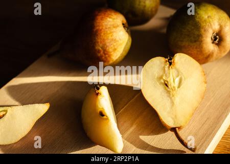 Birnen auf Holztisch bei Sonnenlicht. Reife Birnen und Birnenscheiben auf Holzbrett. Saftige Früchte. Herbstwirtschaft. Herbsternte. Rohe Lebensmittel. Stockfoto