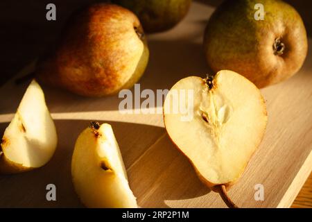 Birnen auf Holztisch bei Sonnenlicht. Reife Birnen und Birnenscheiben auf Holzbrett. Saftige Früchte. Herbstwirtschaft. Herbsternte. Rohe Lebensmittel. Stockfoto