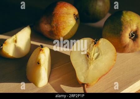 Birnen auf Holztisch bei Sonnenlicht. Reife Birnen und Birnenscheiben auf Holzbrett. Saftige Früchte. Herbstwirtschaft. Herbsternte. Rohe Lebensmittel. Stockfoto
