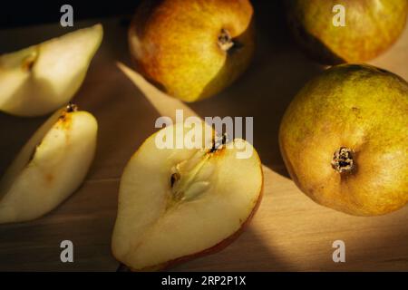 Birnen auf Holztisch bei Sonnenlicht. Reife Birnen und Birnenscheiben auf Holzbrett. Saftige Früchte. Herbstwirtschaft. Herbsternte. Rohe Lebensmittel. Stockfoto