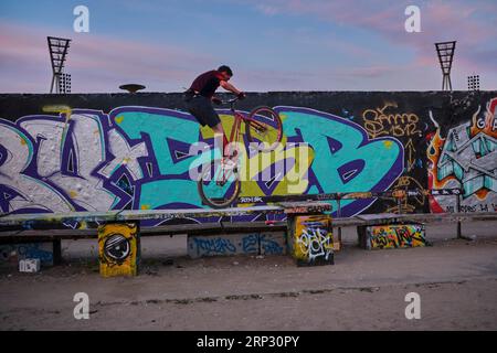 Deutschland, Berlin, 11.06.2023, Sonntagabend im Mauerpark, Radfahrer auf einer Bank an der Graffiti-Mauer Stockfoto