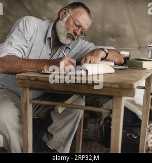 Foto von Ernest Hemingway, der auf seinem Campingplatz in Kenia um 1953 an einem Tisch sitzt und schreibt. Stockfoto