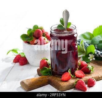 Erdbeermarmelade. Erdbeeren und ein Glas Erdbeermarmelade auf einem weißen Holztisch. Stockfoto