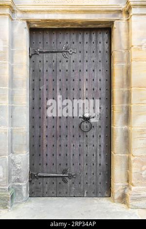 Alte und antike Tür aus braunem Holz mit schwarzen schmiedeeisernen Details. Vertikale Aufnahme. Stockfoto