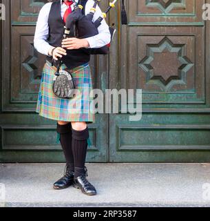 Vorderansicht eines traditionellen schottischen Musikers, der während des Fringe Festivals in Edinburgh, Scotlan, Dudelsack in einem typischen Schottenkotte spielt Stockfoto