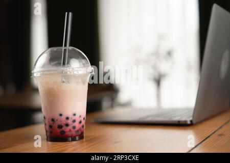 Perlmilchiger Eistee mit Laptop auf Holztisch im Café auf hellem Hintergrund. Leerzeichen kopieren Stockfoto