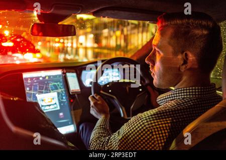 Uber-Fahrer das Rad eines Tesla EV bei Nacht im Regen Stockfoto