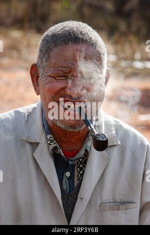 Alter Mann in einem afrikanischen Dorf mit schlechten Zähnen, die traditionelle Pfeife rauchen Stockfoto