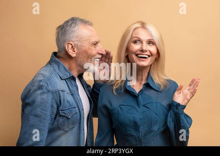 Älterer Mann, der sein Geheimnis mit seiner Frau teilt, beiger Hintergrund Stockfoto