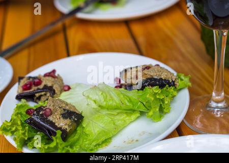 Auberginen-Roulade gefüllt mit Walnüssen und Granatapfelfrüchten mit Knoblauch und georgianischen Gewürzen, serviert auf Salat. Stockfoto