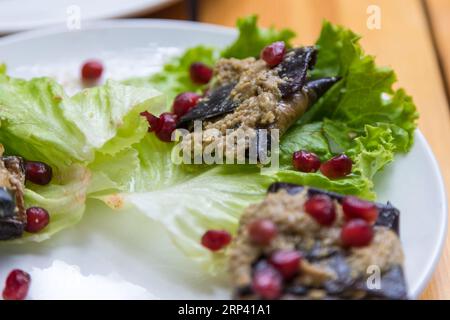 Auberginen-Roulade gefüllt mit Walnüssen und Granatapfelfrüchten mit Knoblauch und georgianischen Gewürzen, serviert auf Salat. Stockfoto