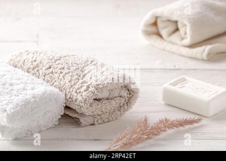 Badaccessoires, Frotteetücher, Seife und trockener Pflanzenzweig auf einem weißen Holztisch. Stockfoto