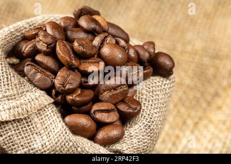 Jutebeutel mit Kaffeebohnen auf einem Hintergrund aus Sackleinen, Nahaufnahme, rustikaler Stil. Stockfoto