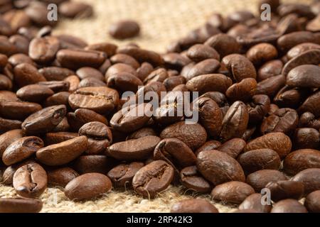 Haufen gerösteter Kaffeebohnen auf Sackleinen-Hintergrund Nahaufnahme. Stockfoto
