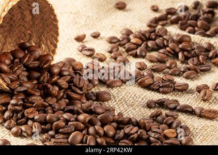 Kaffeebohnen, die aus einem Korb aus Zuckerrohr auf eine Sackleinen-Tischdecke geschüttet wurden. Stockfoto