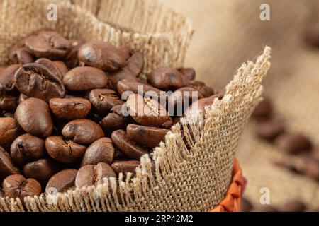 Jutebeutel mit Kaffeebohnen auf einem Hintergrund aus Sackleinen, Nahaufnahme, rustikaler Stil. Stockfoto