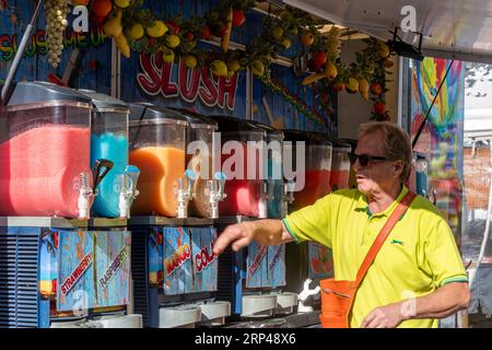 Slush Stand mit Mann, der bunte eiskalte Slushy Fruit Drinks auf einem Markt in Surrey, England, Großbritannien verkauft Stockfoto