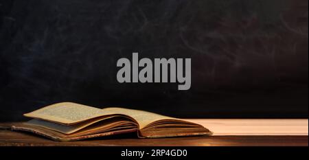 Vintage-Buch auf schwarzem, leerem Tafelhintergrund, Textur. Ledernes Hardcover altes offenes Buch auf Holzschreibtisch. Weisheit, Wissen. Banner, Kopierraum Stockfoto