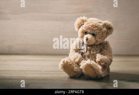 Teddybär sitzt auf einem leeren hölzernen Hintergrund. Braunes, einsames, trauriges, flauschiges Tierspielzeug auf Holztisch. Geburtstag, Valentinstag, Weihnachtsgeschenk. Spac kopieren Stockfoto