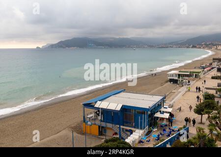 Erhöhter Blick auf die Bucht mit dem leeren Strand und Menschen, die im Winter am Wasser spazieren gehen, Savona, Ligurien, Italien Stockfoto