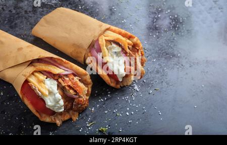 Griechische Gyros in Pita-Brot auf einem schwarzen Gericht verpackt. Leckeres Food-Konzept. Souvlaki, Sawarma mit Fleisch, Zwiebeln, Tomaten, Tzatziki, Kartoffel. Draufsicht Stockfoto