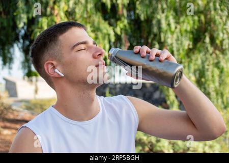 Junger kaukasischer Sportler trinkt aus seiner Wasserflasche, während er Musik mit Ohrhörern hört Stockfoto